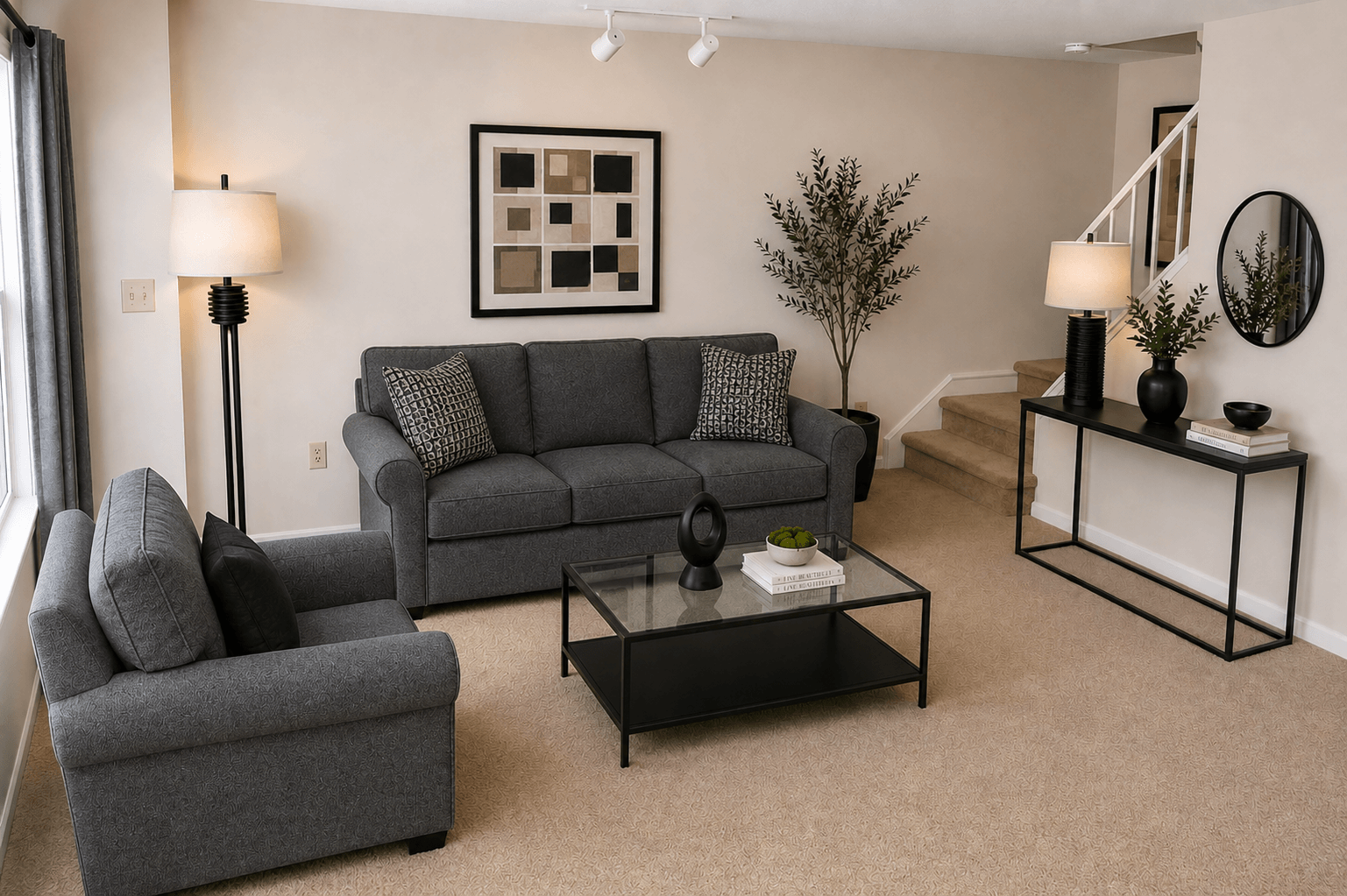 A living room with a grey couch, a grey armchair, a black coffee table, and a small tree.